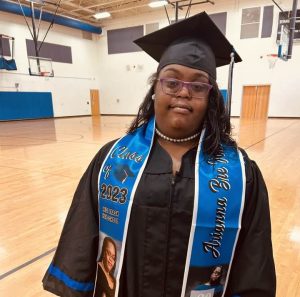 Female student with Down syndrome poses in graduation cap and gown.