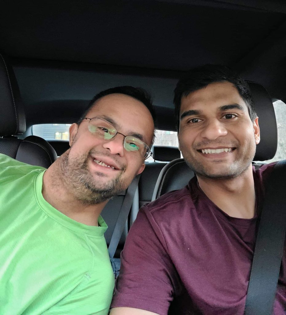 Two men sit side-by-side in a car smiling.